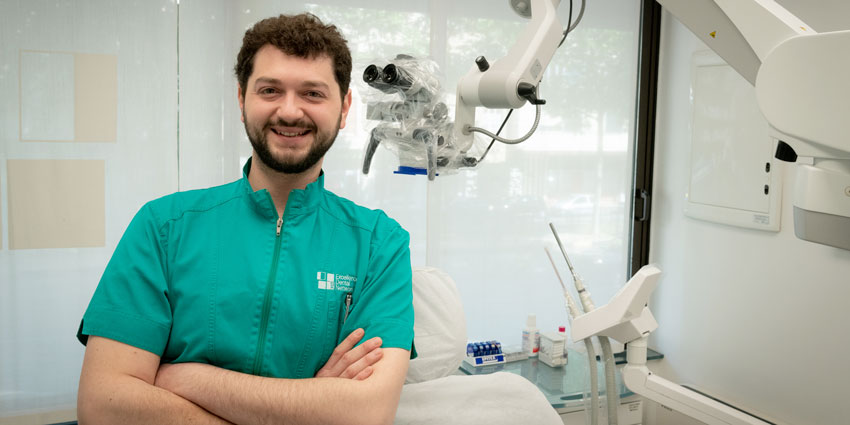 Mezzo busto del giovane dott. Davide Nano, igienista dentale. Il soggetto, a braccia incrociate, si trova nel suo ambiente lavorativo, uno studio odontoiatrico, e indossa una casacca verde con il logo dello studio. Il viso è roseo e sorridente, i capelli e la corta barba curata sono neri e ricci.